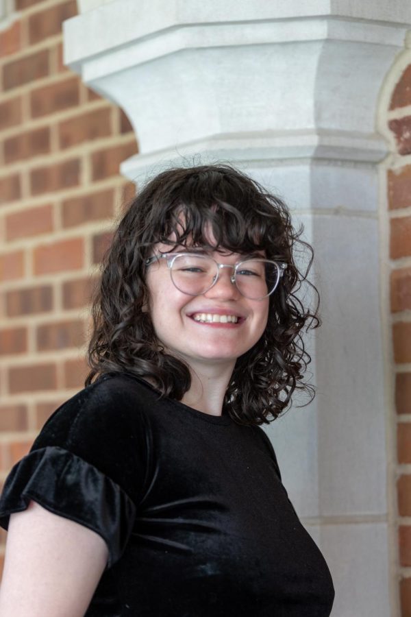 Jessica Barker wearing silver glasses and a black shirt in front of a brick wall