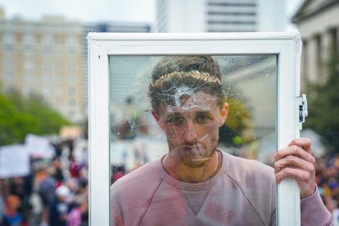 Protestor holds up a pane of glass as if he has been shot through a window, as photographed on April 3, 2023. (Hustler Multimedia/Nikita Rohila)