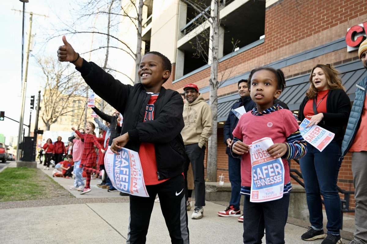 Two children holding Voices for a Safer Tennessee signs cheer on passing by cars honking in solidarity. (Hustler Multimedia/Alysa Suleiman)	