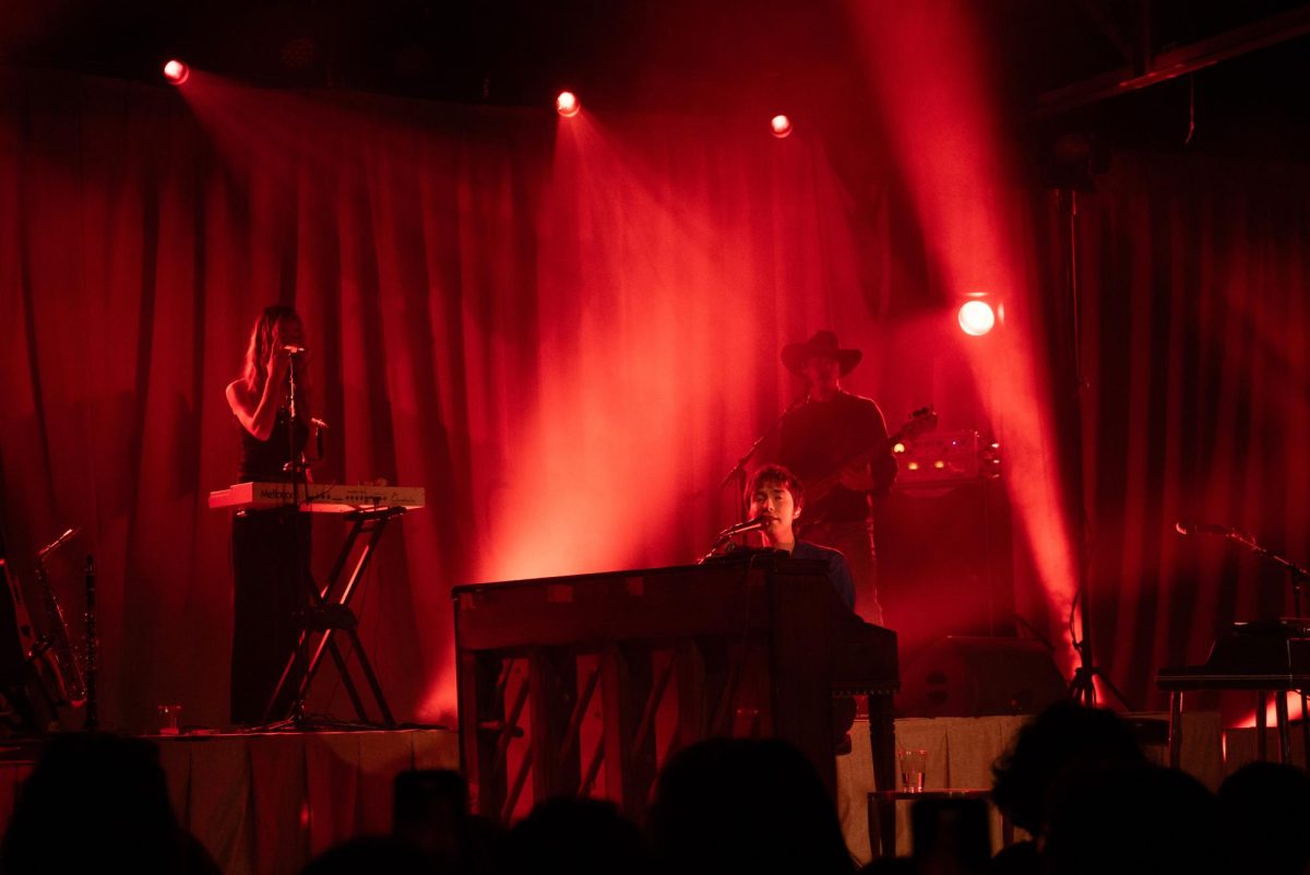Under the red stage lights, Matt Maltese gets the audience to sing along with “As the World Caves In,” as photographed on Sept. 16, 2025. (Hustler Multimedia/Lucas Zhang) 