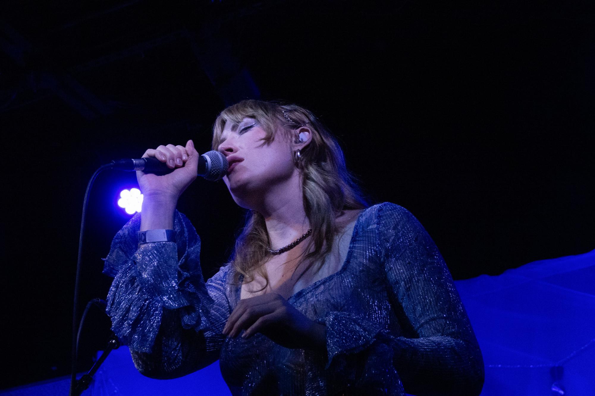 Murr singing into a microphone at The Blue Room, as photographed March 19, 2026. (Hustler Multimedia/Lila Cole)