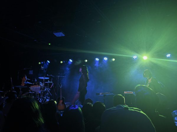 Syd Taylor turns toward her band between songs as green and blue lights fill the stage, as photographed Feb. 27, 2026. (Hustler Multimedia/Naomi Wang)