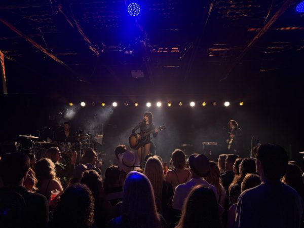 Syd Taylor plays guitar beneath warm stage lights, as photographed Feb. 27, 2026. (Hustler Multimedia/Naomi Wang)