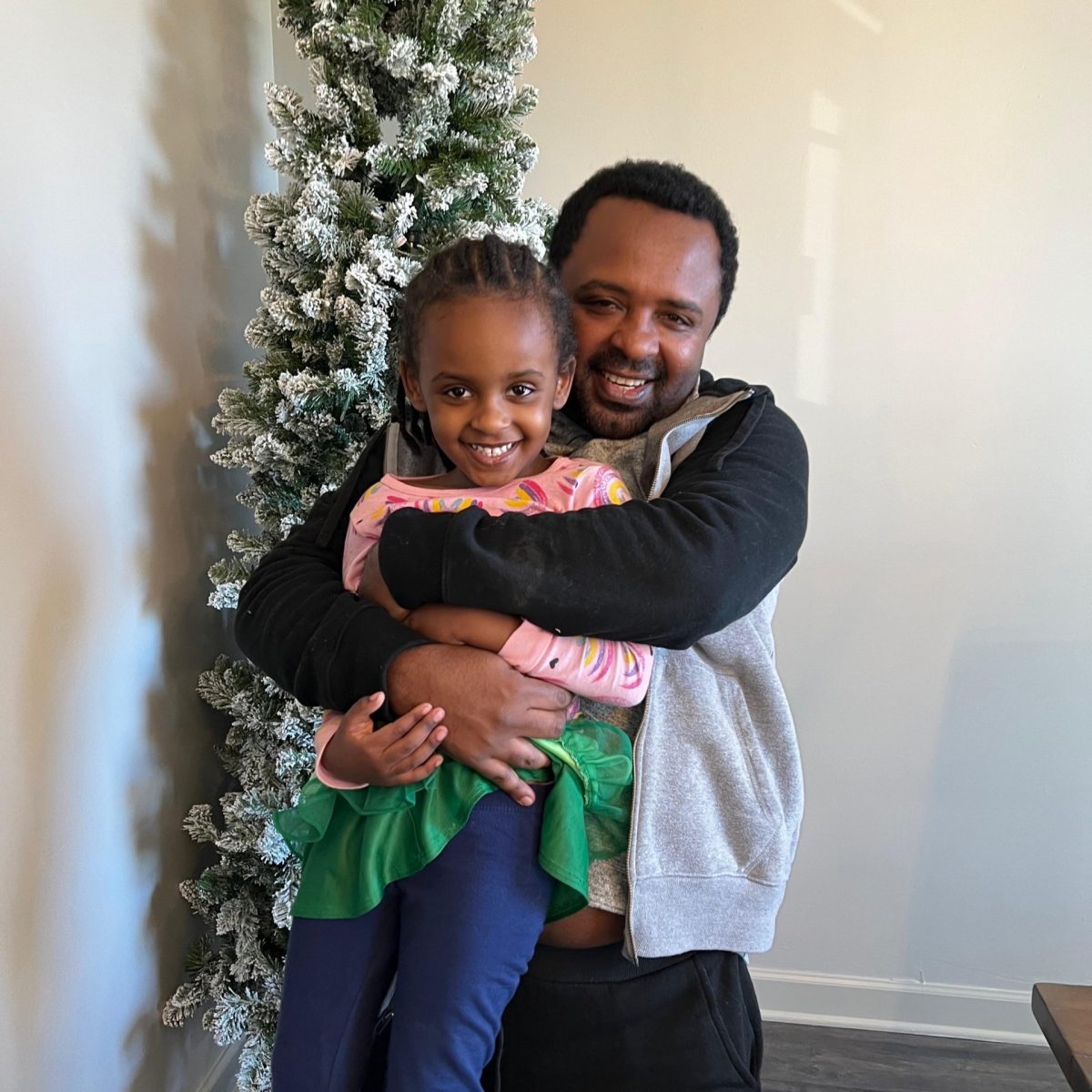 Adugna Olani hugs his daughter in front of a Christmas tree. (Photo courtesy of Meklit Gebre)